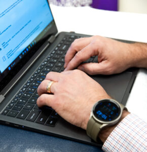 Close-up of Dr. Harrison typing on a laptop during FAA medical exam documentation at Kansas Aviation Medicine.
